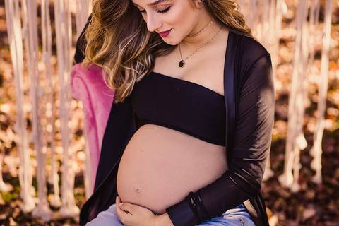 Retrato de gestante loira com a mão na barriga olhando carinhosamente para o bebê'