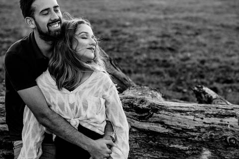 Retrato em preto e branco de casal encostado em tronco de olhos fechados, sentido a brisa, o vento'