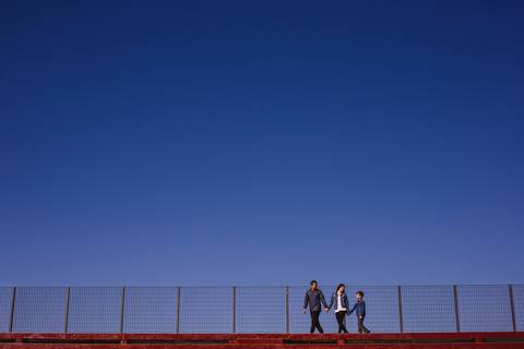 Pai, mãe e filho, caminhando de mãos dadas, com a imensidão do céu azul ao fundo. Família caminhando junto'