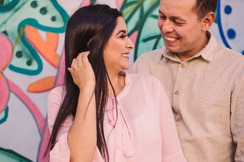 Retrato de casal sorrindo, se olhando, com parede grafitada aos fundos'