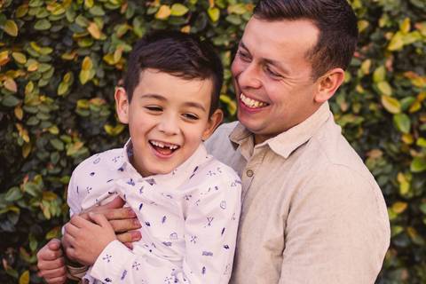 Filho e pai brincando e sorrindo em frente a parede de plantas verdes'