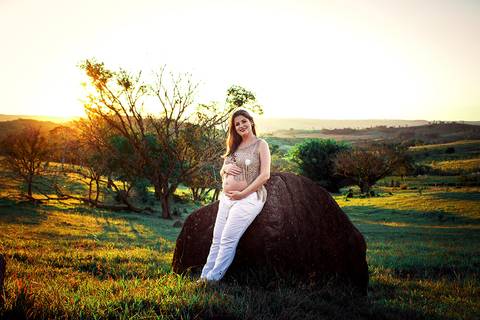 gravida sentada em pedra posando para ensaio de gestante ao por do sol na zona rural de mandaguari na regiao de maringa em campo verde'