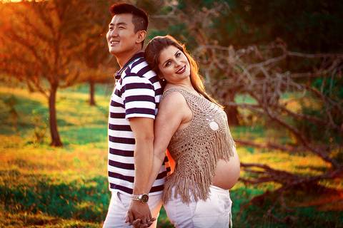 casal sorrindo para camera de costas de mãos dadas em por do sol em ensaio de gestante em campo verde na zona rural de mandaguari na regiao de maringa'