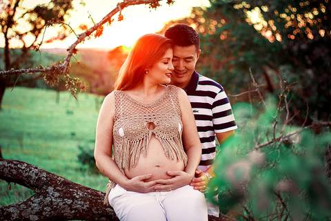 casal sorrindo abraçados sentados em arvore em ensaio de gestante no por do sol na zona rural de mandaguari na regiao de maringa'