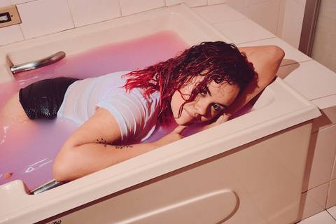 mulher com cabelos molhados debruçada sobre banheira colorida'