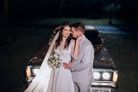 Noivos posam com carinho diante de carro antigo iluminado pela noite. Ensaio de casamento na Casa Irmando em Lajeado. Foto por Alba Estúdio.'