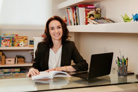 Psicopedagoga Aline sentada à mesa de trabalho com laptop aberto'