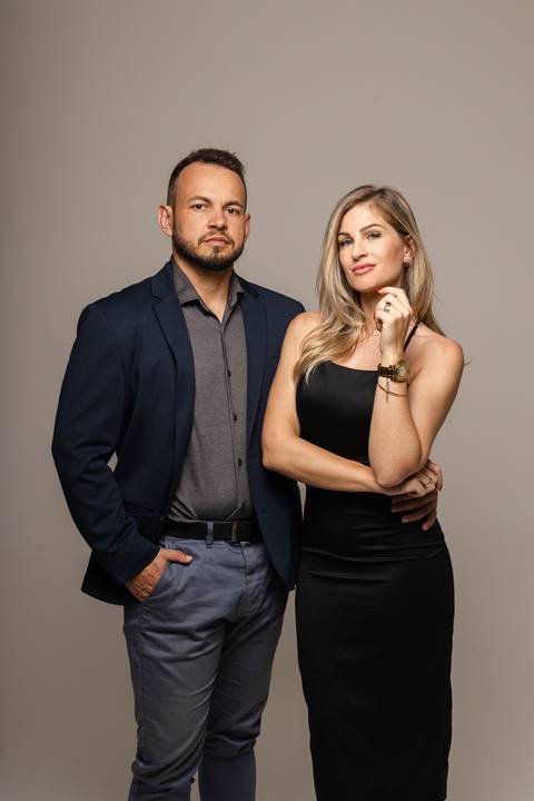 Michele e Vinícius posam lado a lado em estúdio com fundo cinza neutro'