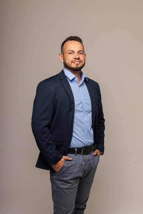 Vinícius em retrato corporativo, vestindo paletó azul contra fundo neutro'