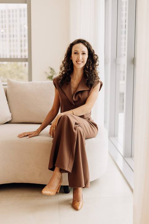 Retrato corporativo da psicóloga sentada em sofá, ensaio de posicionamento de marca pessoal em ambiente clean no estúdio em Lajeado.'