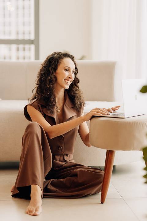 Psicóloga em pose descontraída no chão, digitando no notebook em ensaio de posicionamento minimalista no estúdio em Lajeado.'