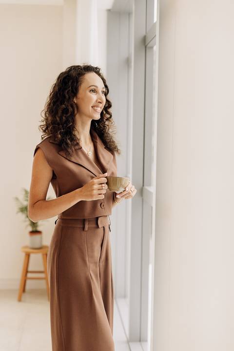 Psicóloga em ensaio de posicionamento, segurando uma xícara e olhando pela janela, estúdio minimalista em Lajeado – Alba Estúdio.'