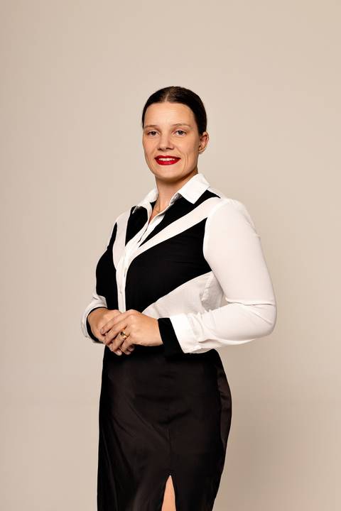 Mulher de pé, vestindo camisa branca com detalhes pretos geométricos, pôr do batom vermelho, fundo bege uniforme'