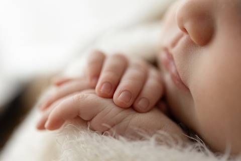 “Close-up das pequenas mãos do bebê apoiadas sobre tecido felpudo”'