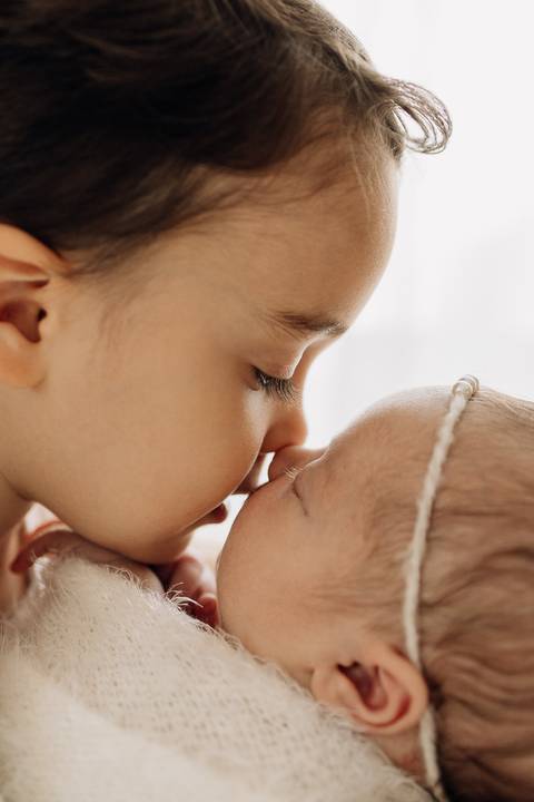 “Irmão mais velho dando um beijo carinhoso no nariz da irmã recém-nascida”'