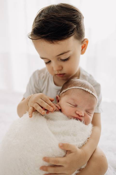 “Irmão segura a irmã recém-nascida enrolada em manta felpuda”'