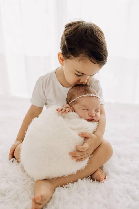 “Olhar terno do irmão mais velho sobre recém-nascida enrolada em manta”'