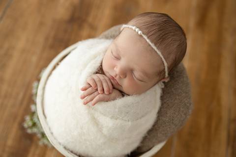 “Recém-nascida dormindo em balde de madeira forrado com manta branca”'