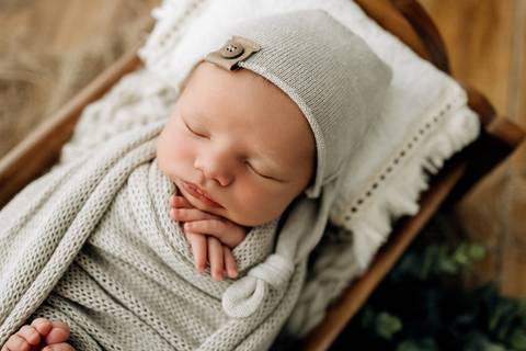 Bebê Lorenzo dormindo em mini cama de madeira, enrolado em manta bege clara e touca de tricô, fotografia newborn no Alba Estúdio.'