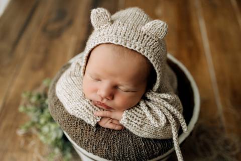 Retrato newborn do bebê Lorenzo com gorro de tricô bege com orelhinhas, apoiado no balde, fotografia no Alba Estúdio.'