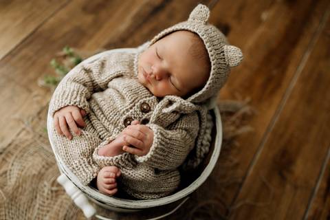 Bebê Lorenzo deitado dentro do balde branco, vestido com macacão de tricô bege, ensaio newborn no Alba Estúdio.'