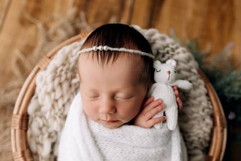 Foto newborn em Lajeado – recém-nascida dormindo enrolada em manta branca, segurando ursinho de tricô, fotografia feita pelo Alba Estúdio.'