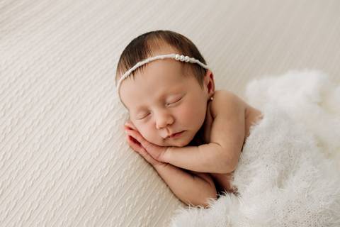 Foto newborn em Lajeado – recém-nascida dormindo enrolada em manta branca, com tiara de pérolas, fotografia feita no Alba Estúdio.'