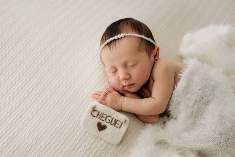 Ensaio newborn em Lajeado – recém-nascida dormindo em manta branca com plaquinha “Cheguei”, fotografia feita pelo Alba Estúdio.'