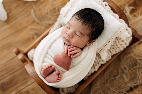 Bebê Noah no ensaio newborn enrolado em manta clara, segurando coração de feltro vermelho, no estúdio Alba Estúdio em Lajeado.'