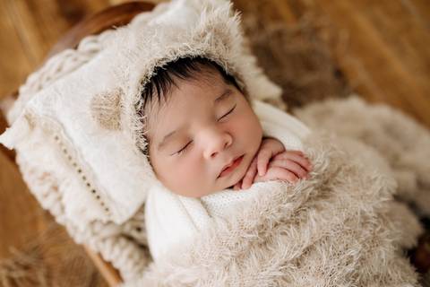 Bebê Noah no ensaio newborn, enrolado em manta e usando gorro felpudo com orelhinhas, deitado em mini cama no estúdio Alba Estúdio em Lajeado.'