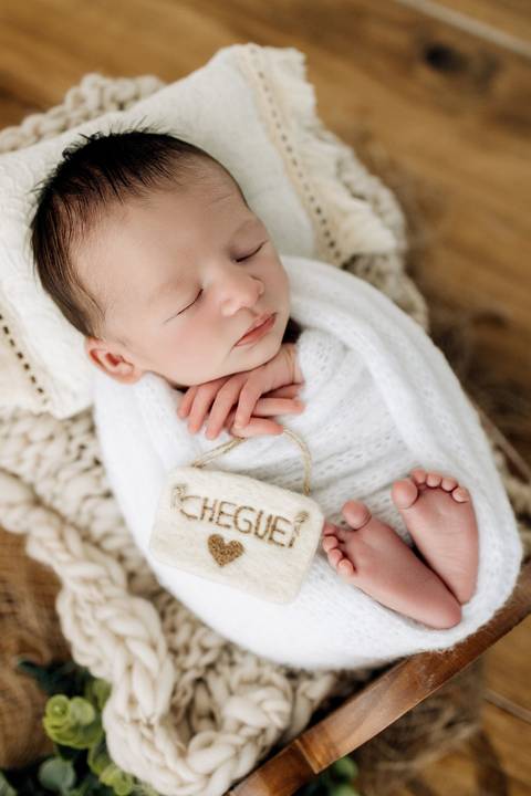 Foto newborn do bebê Vicente dormindo, enrolado em manta branca e deitado em mini cama no estúdio Alba Estúdio em Lajeado.'