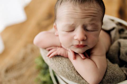 Foto newborn em Lajeado – bebê recém-nascido dormindo dentro de balde branco, apoiado em manta bege, com fundo de madeira. Ensaio feito pelo Alba Estúdio.'