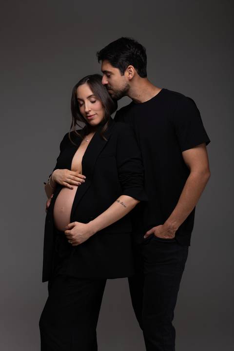 Retrato afetivo de casal em ensaio gestante, com beijo na cabeça e mãos envolvendo a barriga na espera por Pietro. Fotografia elegante do Alba Estúdio em Lajeado, RS.'
