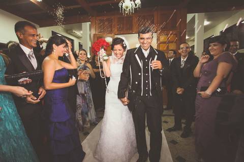 Noiva e noivo saindo da cerimônia religiosa na Igreja Nossa Senhora da Saúde em Casimiro de Abreu RJ sob chuva de arroz'