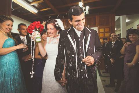 Noiva e noivo saindo da cerimônia religiosa na Igreja Nossa Senhora da Saúde em Casimiro de Abreu RJ sob chuva de arroz'