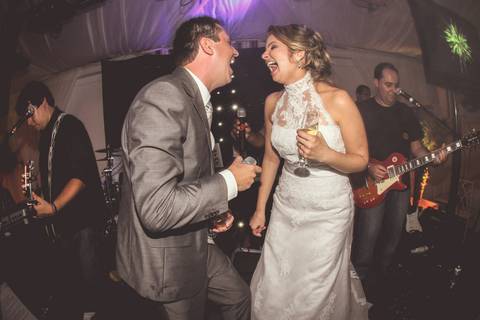 Noivo e noiva cantam durante a Recepção acompanhados de banda em foto colorida'