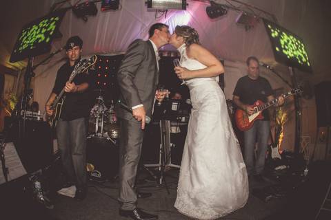 Noivo e noiva dão beijo durante a Recepção acompanhados de banda em foto colorida'