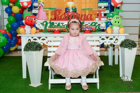 Ramona num vestido cor de rosa de princesa, está sentada em um banco de madeira branco, isso no clique de by Eli Matos'