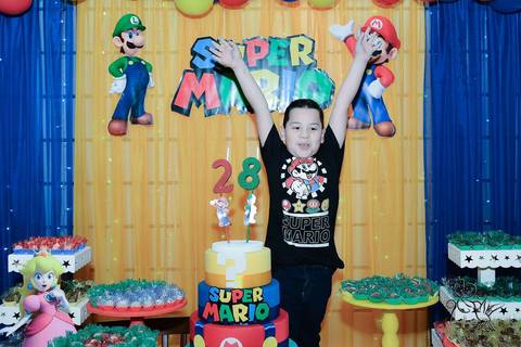 Victor abre os braços na frente do painel decorado com o tema Super Mario na sua festa de oito anos, clique de by Eli Matos'
