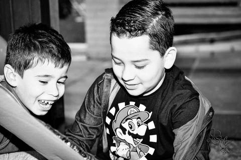 Meninos sorriem ao abrir o pacote e ver ver o brinquedo que estava nele, foto em preto e branco de by Eli Matos'