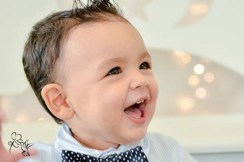 Eduardo sorri com calça azul,camisa branca e gravata borboleta azul no seu aniversário de um ano, by Eli Matos registrou'