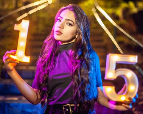 debutante  sentada  em uma escada  com luzes  coloridas  rosa e azul '