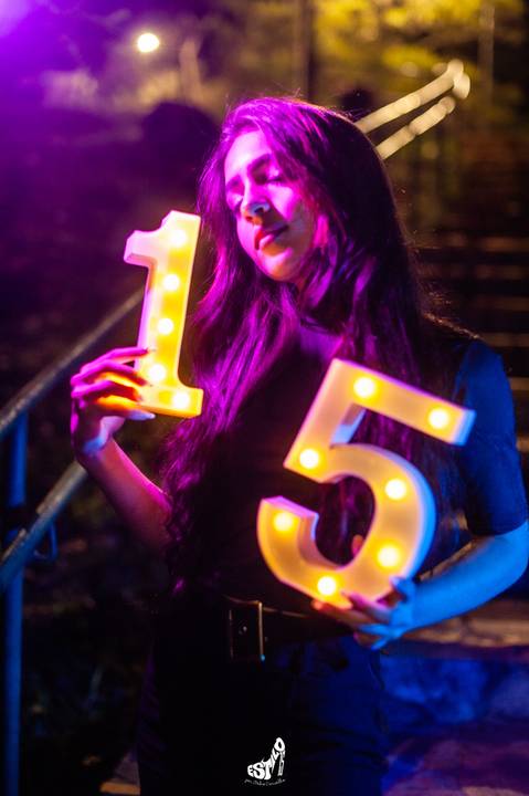 debutante  sentada  em uma escada  com luzes  coloridas  rosa e azul '