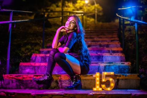 debutante  sentada  em uma escada  com luzes  coloridas  rosa e azul '