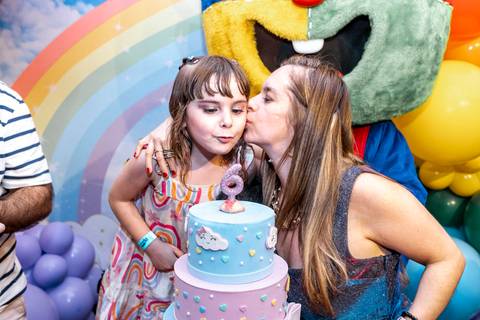 Fotografia de família em aniversário: mãe beija a filha com carinho após o parabéns, em festa infantil realizada no Plus Buffet em São Paulo.'
