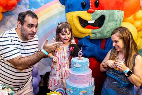 Fotojornalismo de aniversário infantil: família reage com alegria e surpresa na hora do parabéns, com o mascote do Plus Buffet ao lado, em festa em São Paulo.