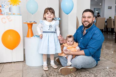 Foto de festa de aniversário infantil no Tatuapé, mostrando o pai com a aniversariante Alice e sua irmã bebê na decoração da Bluey.'