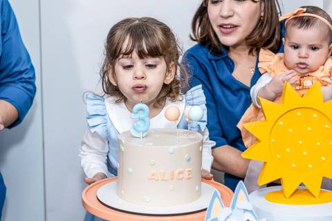 Foto de festa de aniversário infantil no Tatuapé, com a aniversariante Alice soprando a vela de 3 anos em seu bolo do tema Bluey.'