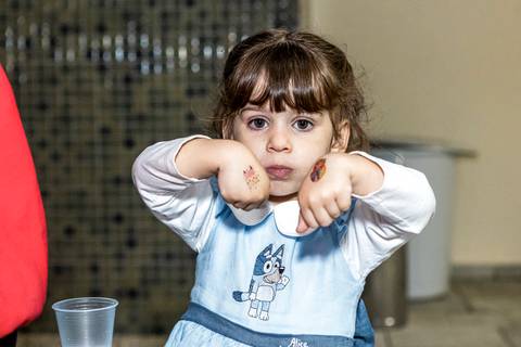 Foto de festa de aniversário infantil no Tatuapé, com a aniversariante Alice mostrando suas tatuagens temporárias para a câmera.'