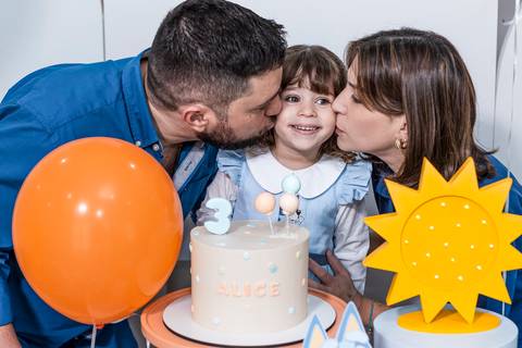 Foto de festa de aniversário infantil com a aniversariante Alice recebendo beijo dos pais na mesa do bolo, tema Bluey, registrada por fotógrafo de aniversário infantil no Tatuapé.'